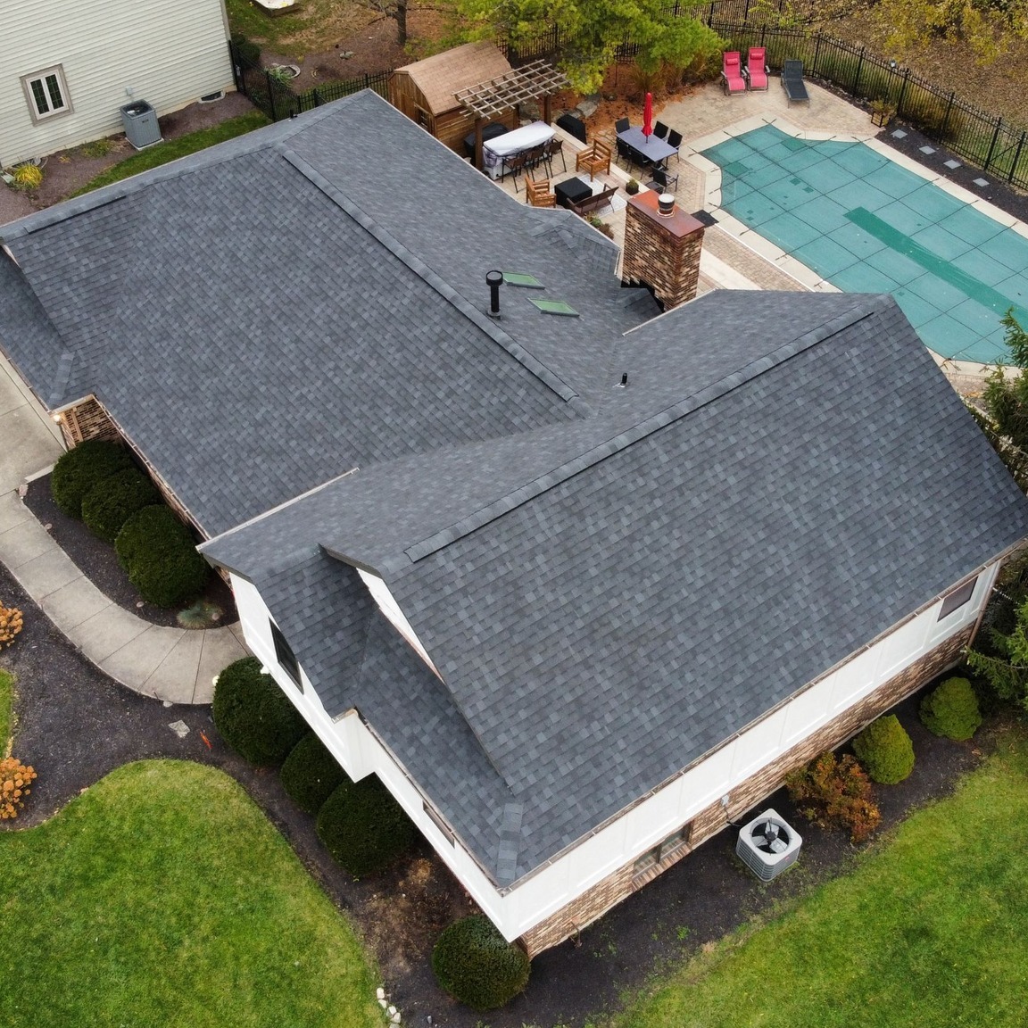 Aerial view of a home with a new dark gray asphalt shingle roof, a brick chimney and a backyard pool