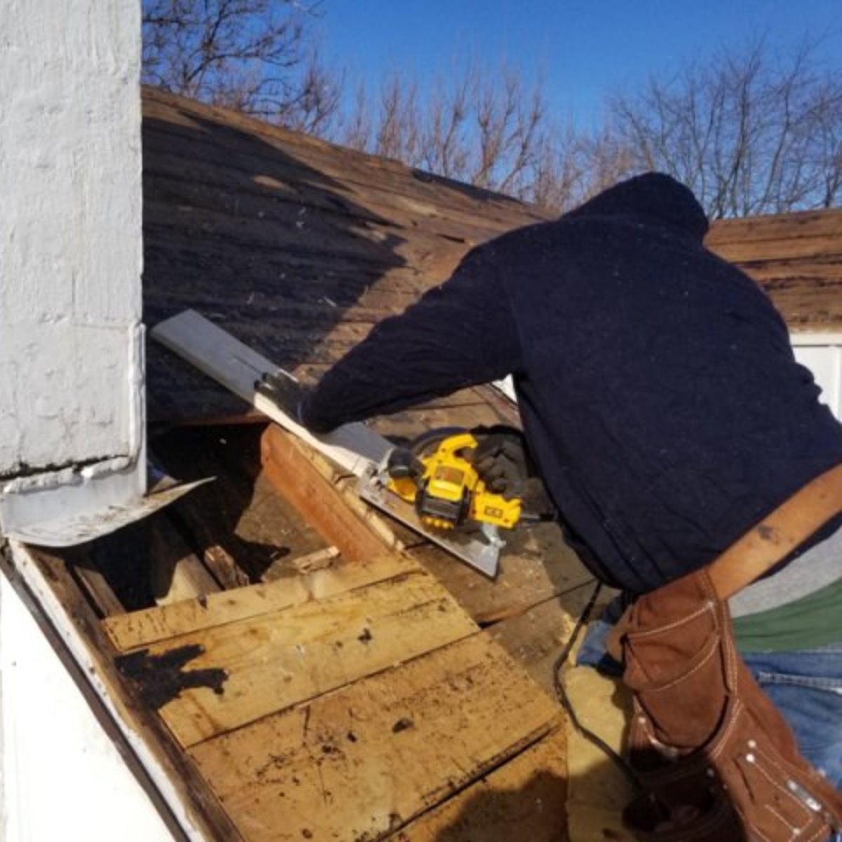 Roofer cutting out damaged roof decking with a circular saw beside a chimney during a roof repair
