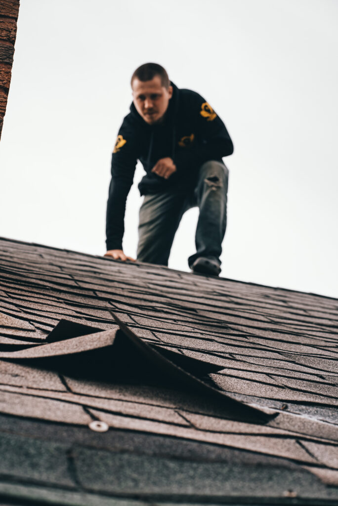 Roofing contractor inspecting lifted asphalt shingles during a residential roof repair