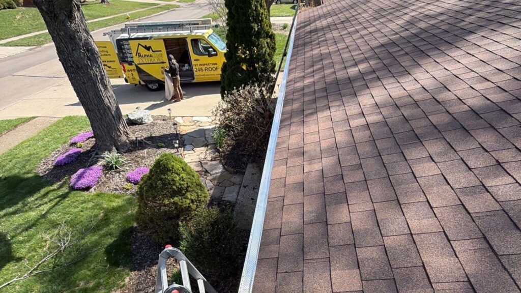 Gutter guard installation in Kettering Ohio with roofing contractor inspecting roof and gutters beside AlphaOne Exteriors service van