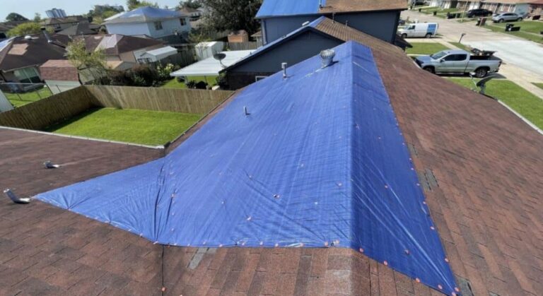 Aerial view of a blue emergency tarp weighted down over a section of shingle roof