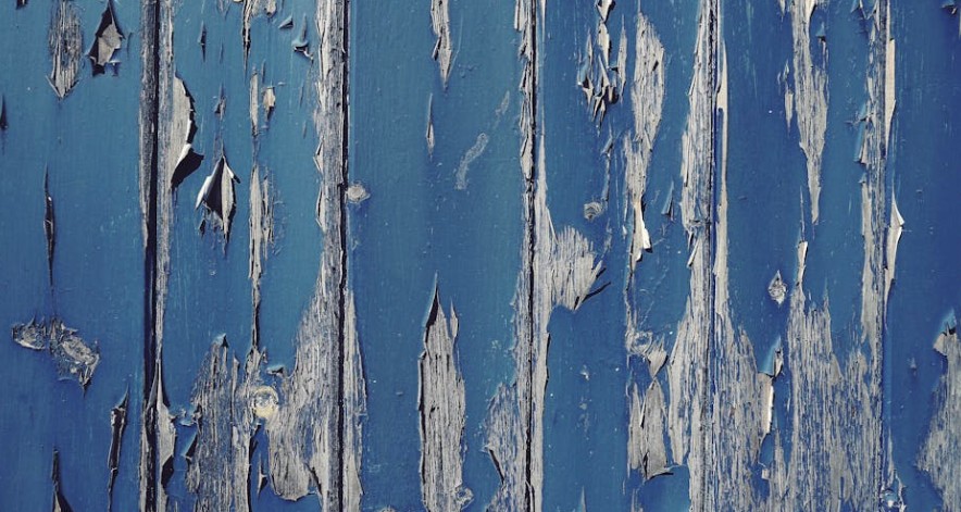 Peeling and cracking blue exterior paint on old wood siding showing severe paint failure and weather damage on a home exterior in Dayton, Ohio.
