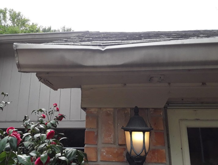 White gutter with a visible dent running along a low roof eave above board-and-batten siding on a home in Dayton, Ohio