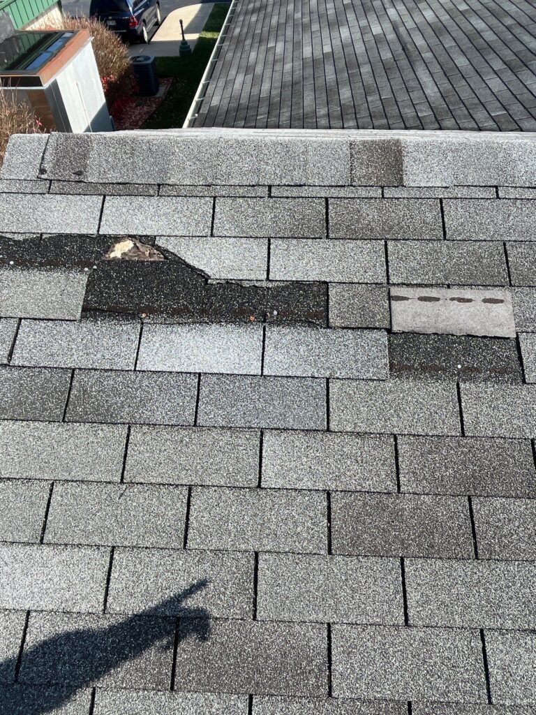 Wind-damaged asphalt roof shingles on a home in Englewood, Ohio showing torn and missing shingle tabs caused by high winds.