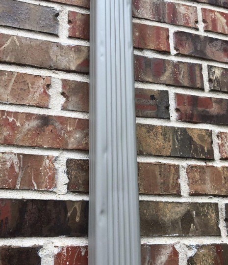 Aluminium downspout running down a brick wall on a home in Miamisburg, Ohio, with shallow hail dents across its face