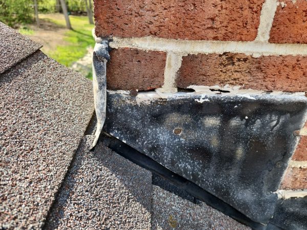 Failing chimney flashing in Kettering Ohio showing cracked sealant and potential roof leak at brick chimney